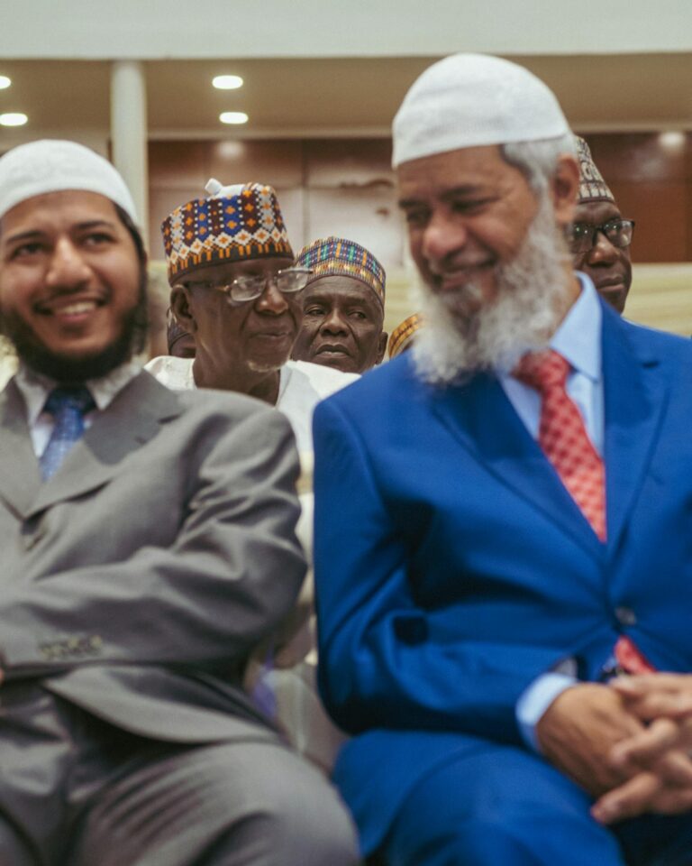 A diverse group of men in traditional and business attire at a meeting, smiling together.
